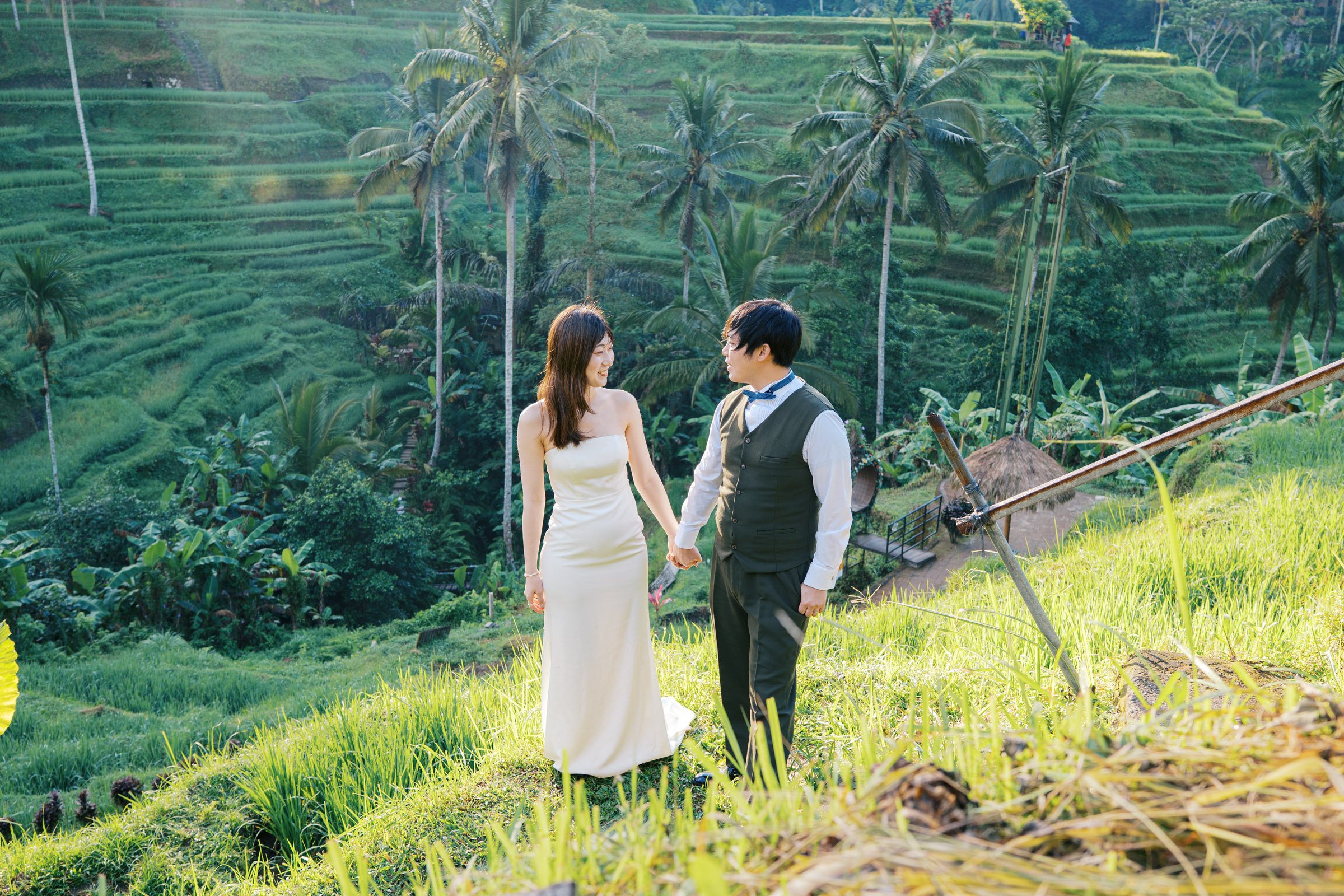 Tatsu and Mika holding hands with green rice terraces and palm trees behind them