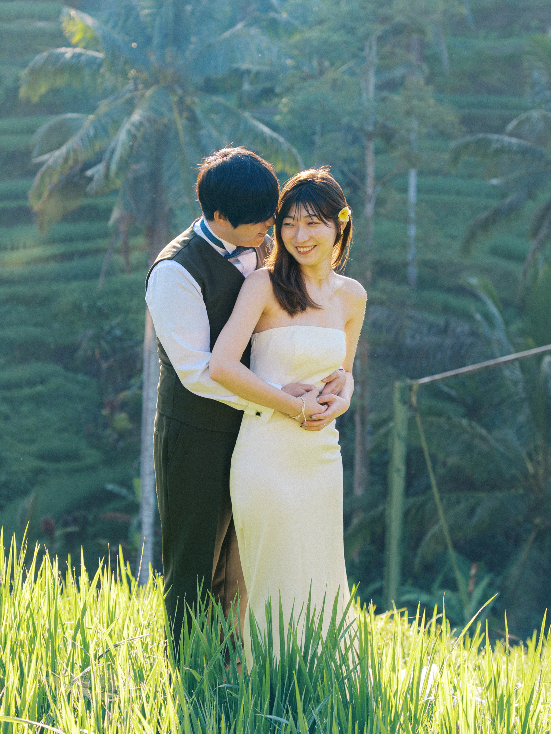 Tatsu and Mika smiling together in an embrace with palm trees behind them